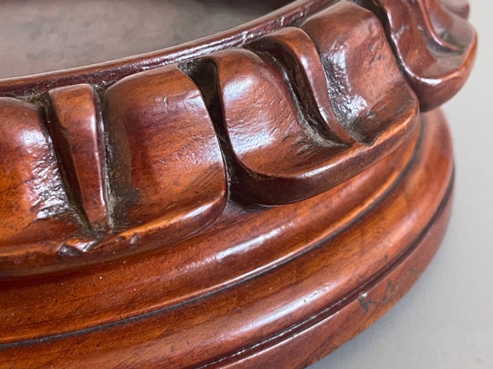 A circular carved brown wooden wine coaster featuring a fluted rim and a recessed circular centre. View II