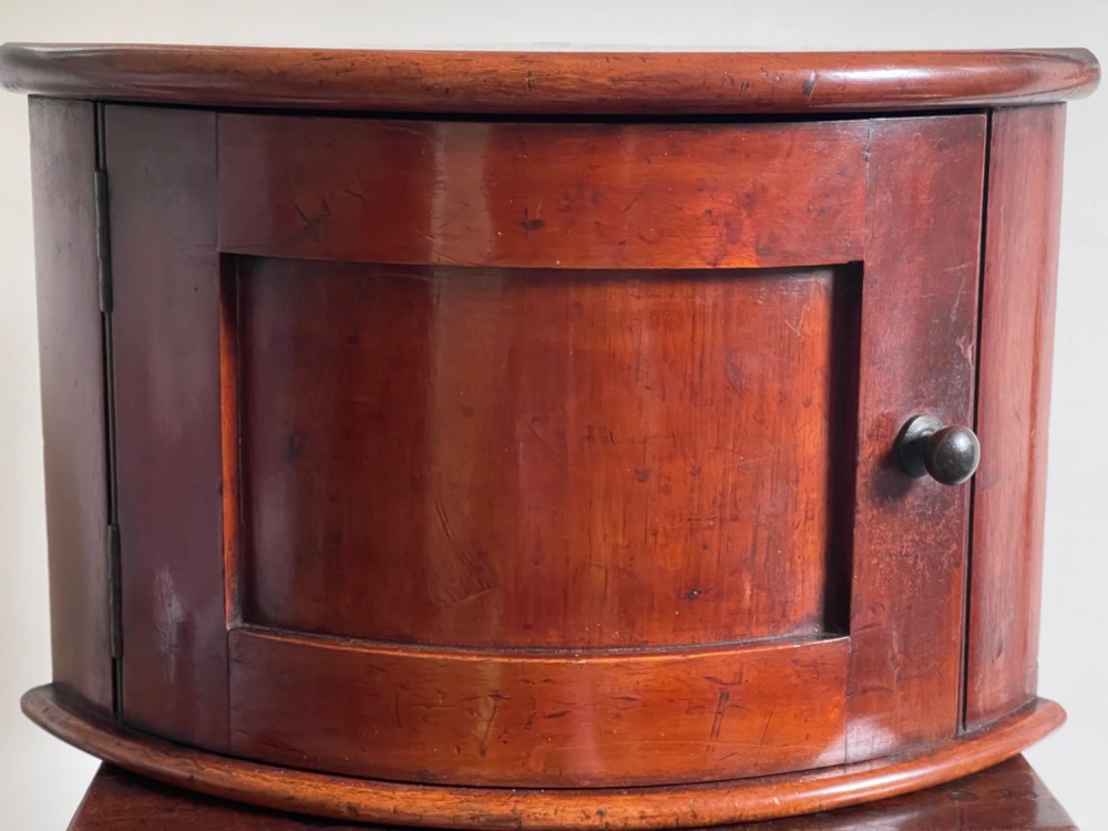 A small bowfront mahogany corner cupboard featuring a single curved door with a recessed panel and a turned wooden knob.