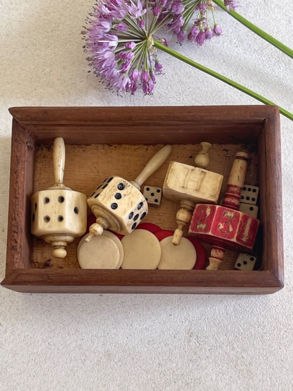 A rectangular wooden box holding hand-carved bone teetotum spinning tops, miniature dice, and red and white counter discs. View IV