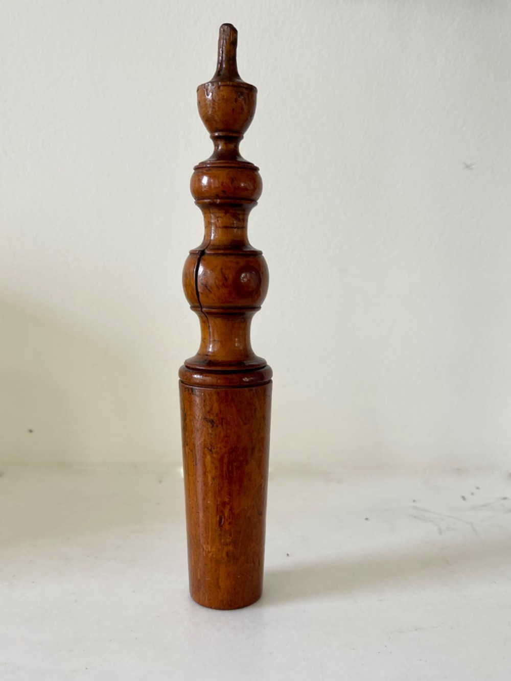 A hand-turned antique wooden childs rattle featuring turned baluster detailing and a tapered cylindrical base with a warm polished finish. View II