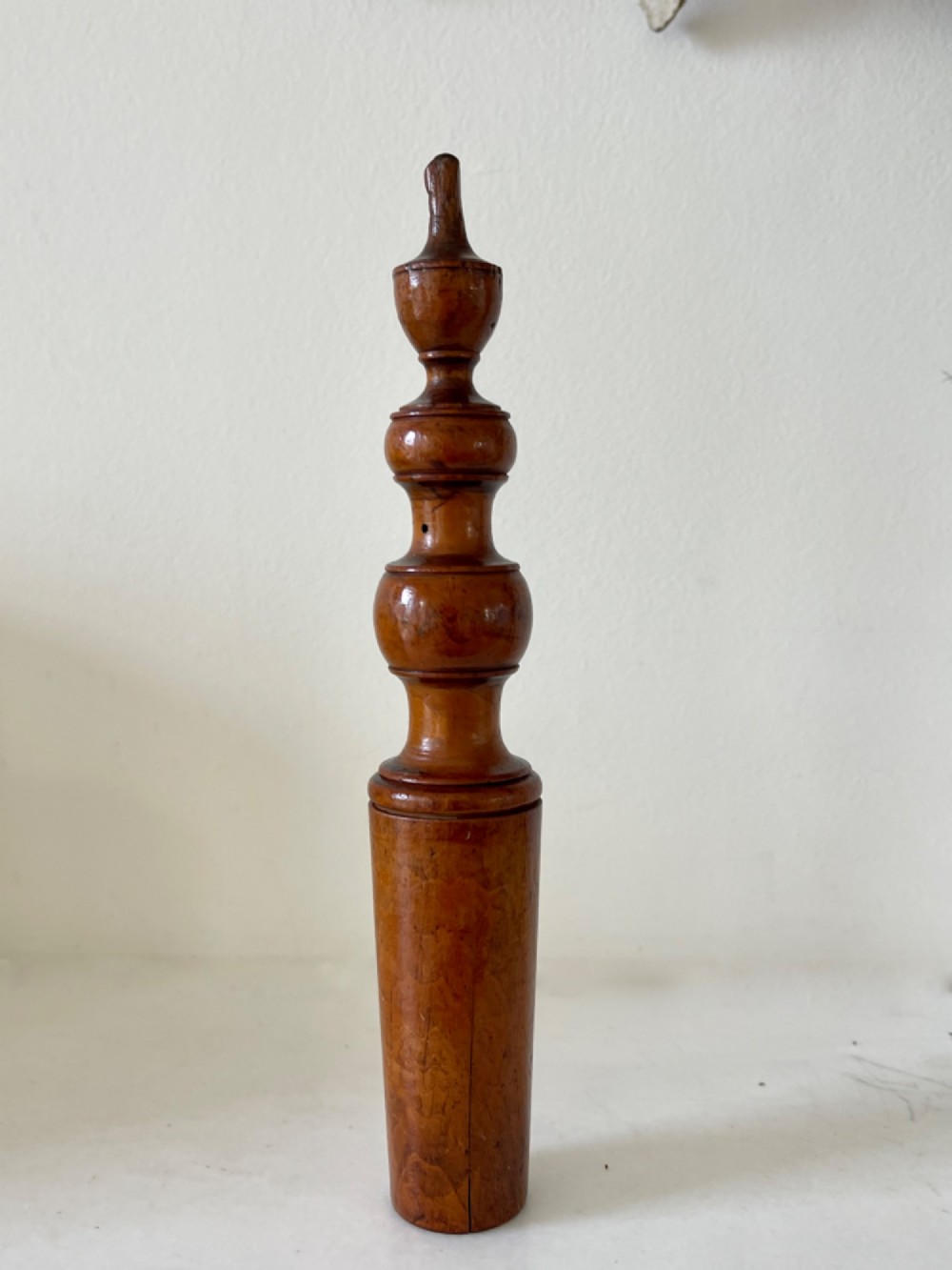 A hand-turned antique wooden childs rattle featuring turned baluster detailing and a tapered cylindrical base with a warm polished finish. View III