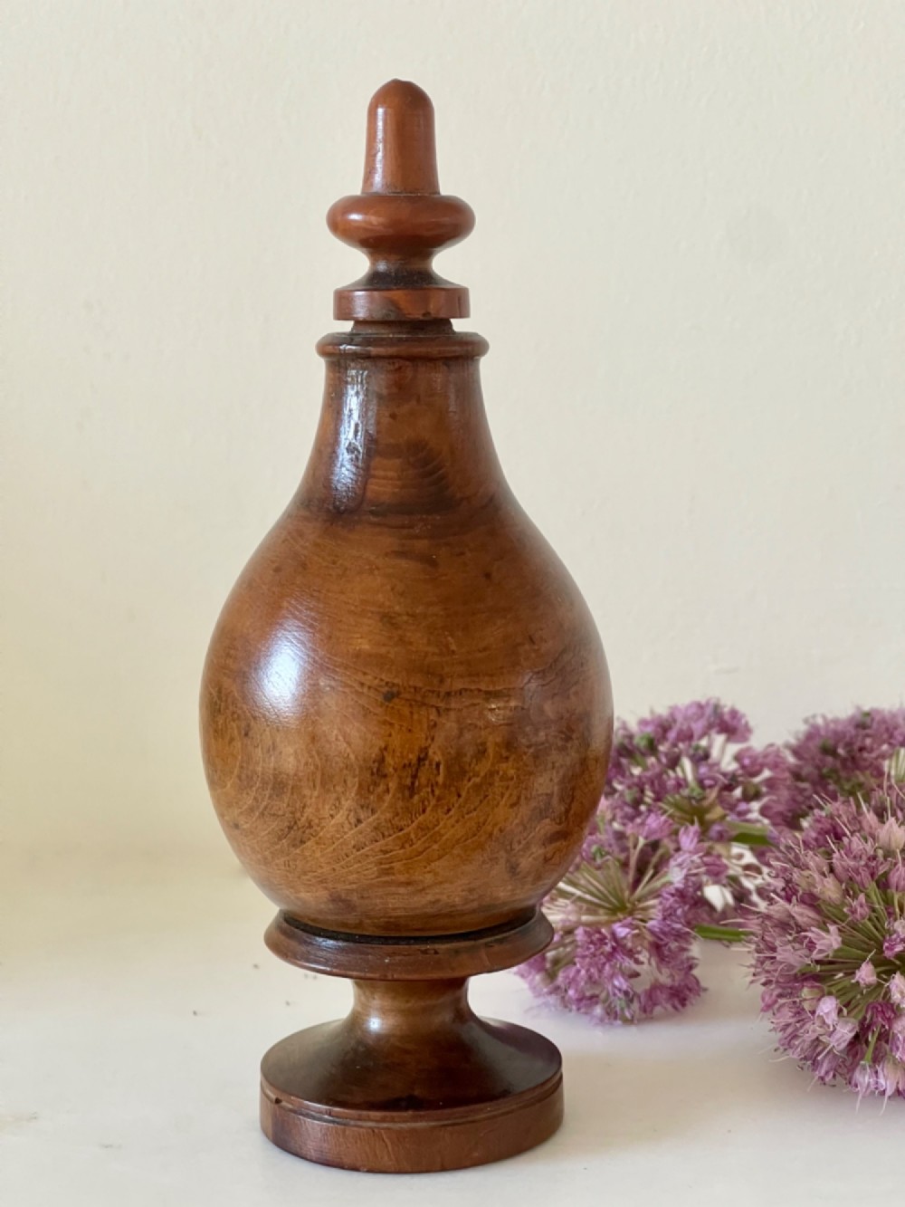 A turned brown hardwood spice flask featuring a bulbous body, finial stopper, and a stepped circular pedestal base.