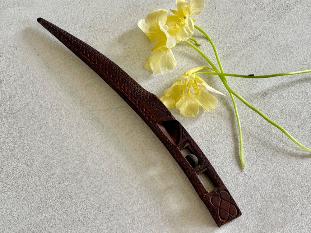 A dark hand-carved wooden treen knitting sheath featuring geometric chip carving, a ball-in-cage detail, and a carved heart motif.