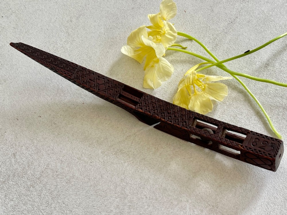 A dark hand-carved wooden treen knitting sheath featuring geometric chip carving, a ball-in-cage detail, and a carved heart motif. View IV