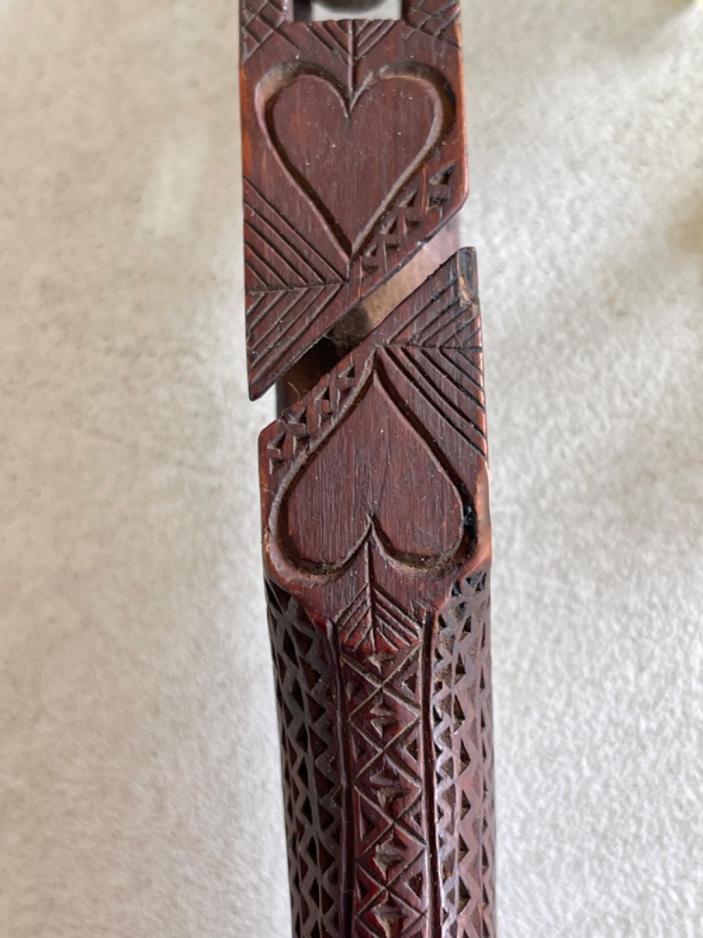 A dark hand-carved wooden treen knitting sheath featuring geometric chip carving, a ball-in-cage detail, and a carved heart motif. View VII