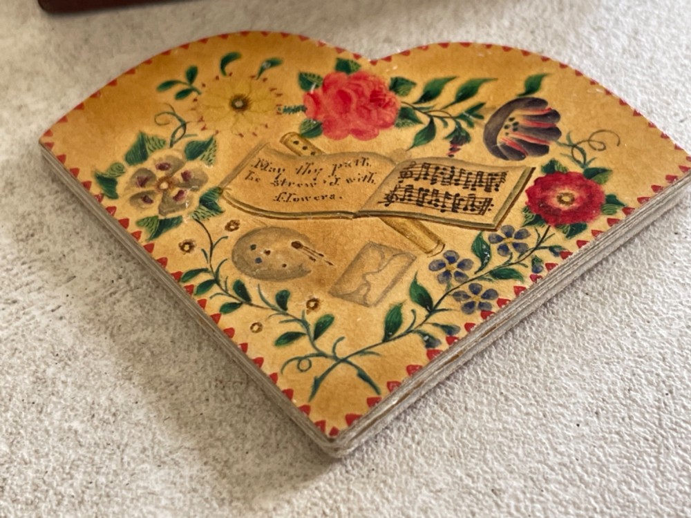 An open small wooden box containing printed paper riddle slips set behind a heart-shaped printed card with floral motifs. View II