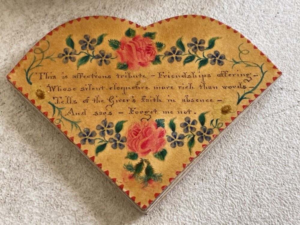 An open small wooden box containing printed paper riddle slips set behind a heart-shaped printed card with floral motifs. View V