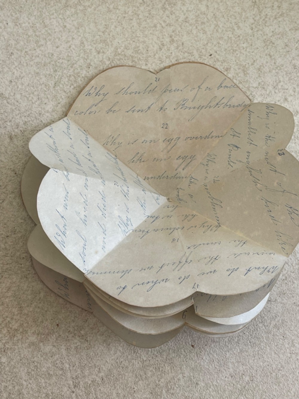 An open small wooden box containing printed paper riddle slips set behind a heart-shaped printed card with floral motifs. View VII