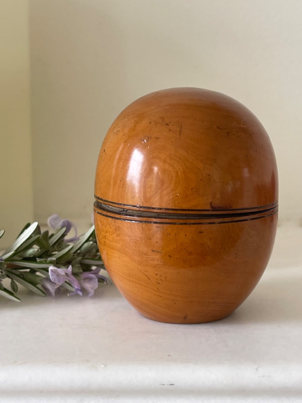 A smooth, egg-shaped turned wooden antique pill silverer featuring a central joining seam and a warm polished grain finish.