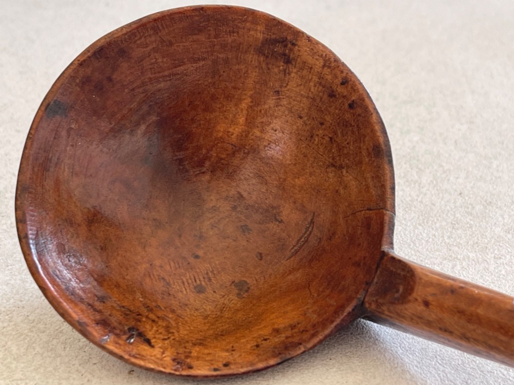 A hand-carved antique treen wooden ladle featuring a deep circular bowl and a shaped handle with decorative notched detailing. View II