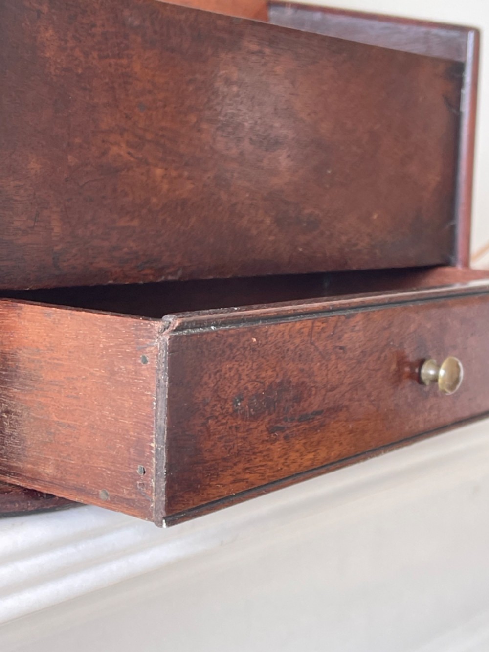 An antique dark mahogany wooden candle box featuring a shaped backboard with a hanging hole, a hinged top lid, a lower drawer with a metal knob, and a shaped apron base. View III