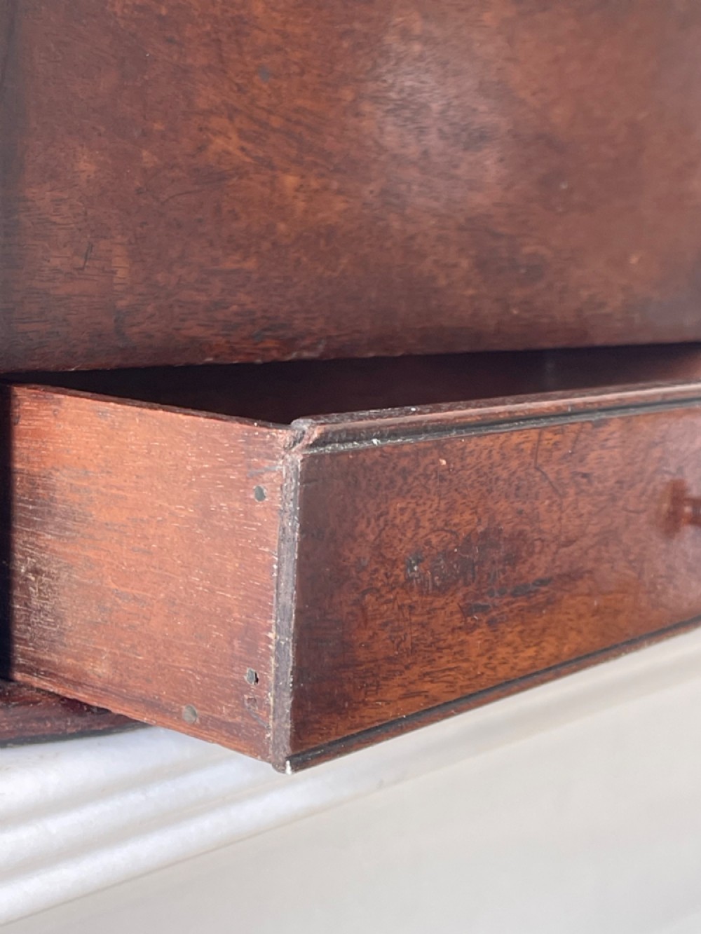 An antique dark mahogany wooden candle box featuring a shaped backboard with a hanging hole, a hinged top lid, a lower drawer with a metal knob, and a shaped apron base. View V