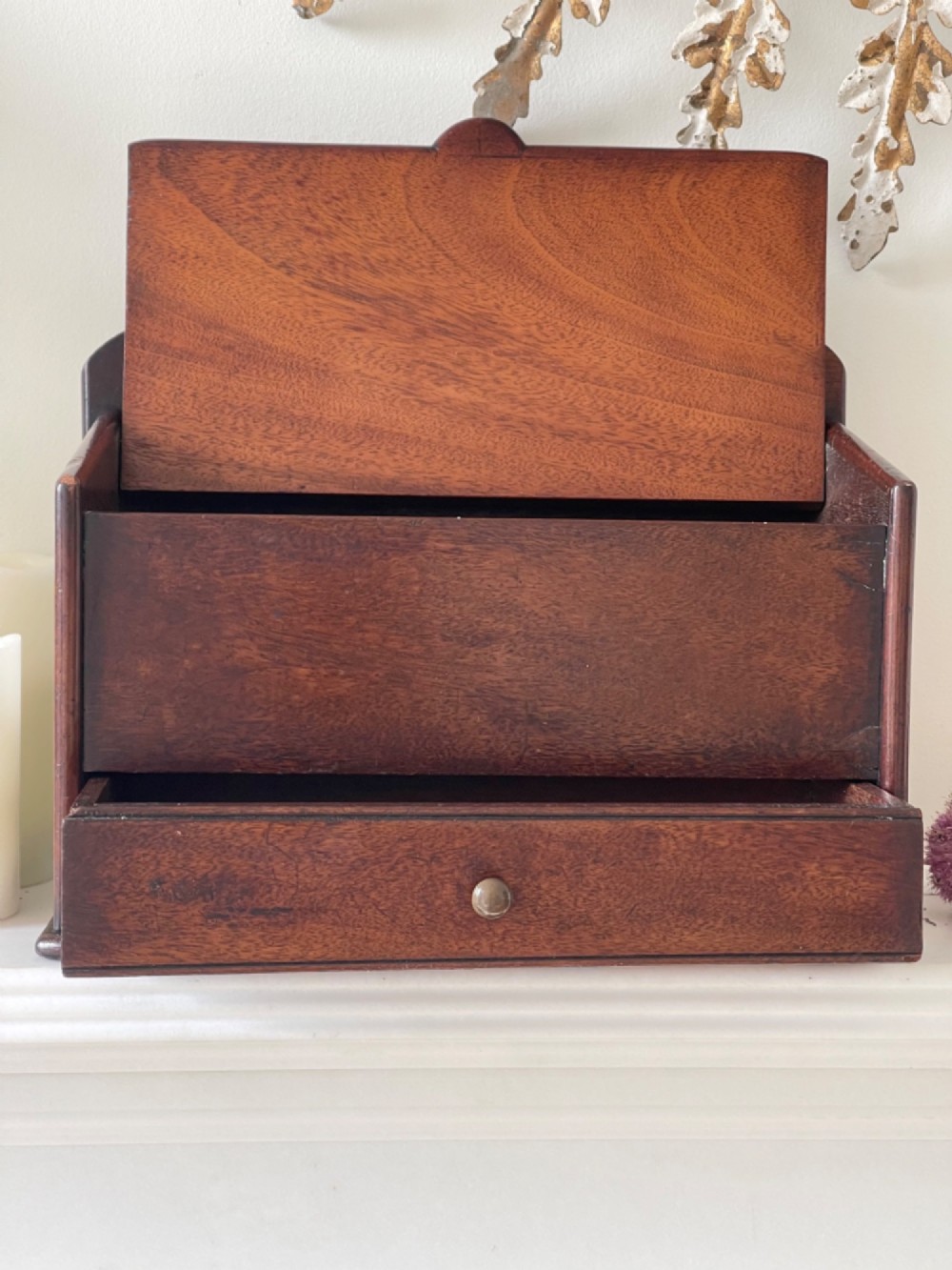 An antique dark mahogany wooden candle box featuring a shaped backboard with a hanging hole, a hinged top lid, a lower drawer with a metal knob, and a shaped apron base. View VI