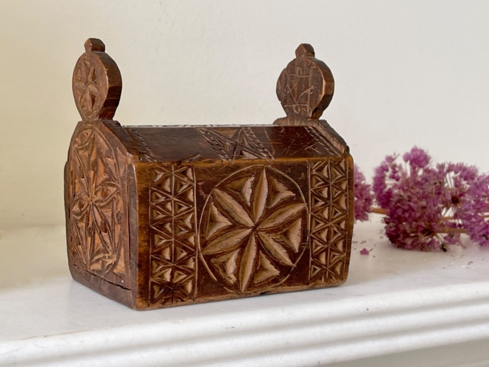 A small hand-carved warm brown wooden box featuring geometric chip-carved starburst motifs and upright carved finials.