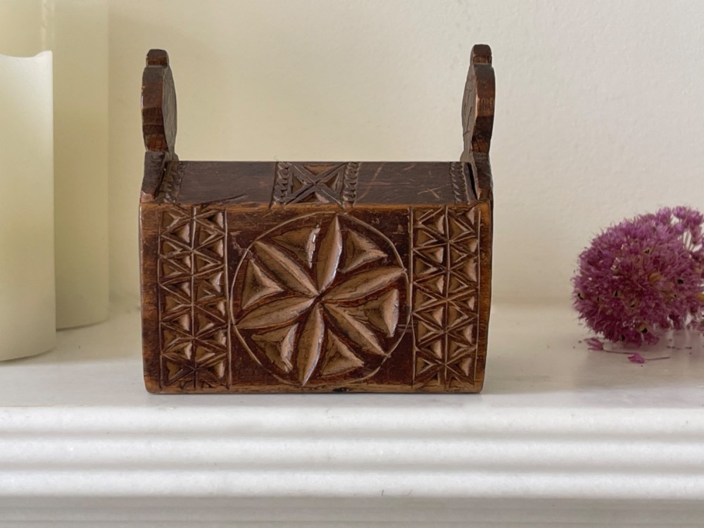 A small hand-carved warm brown wooden box featuring geometric chip-carved starburst motifs and upright carved finials. View II