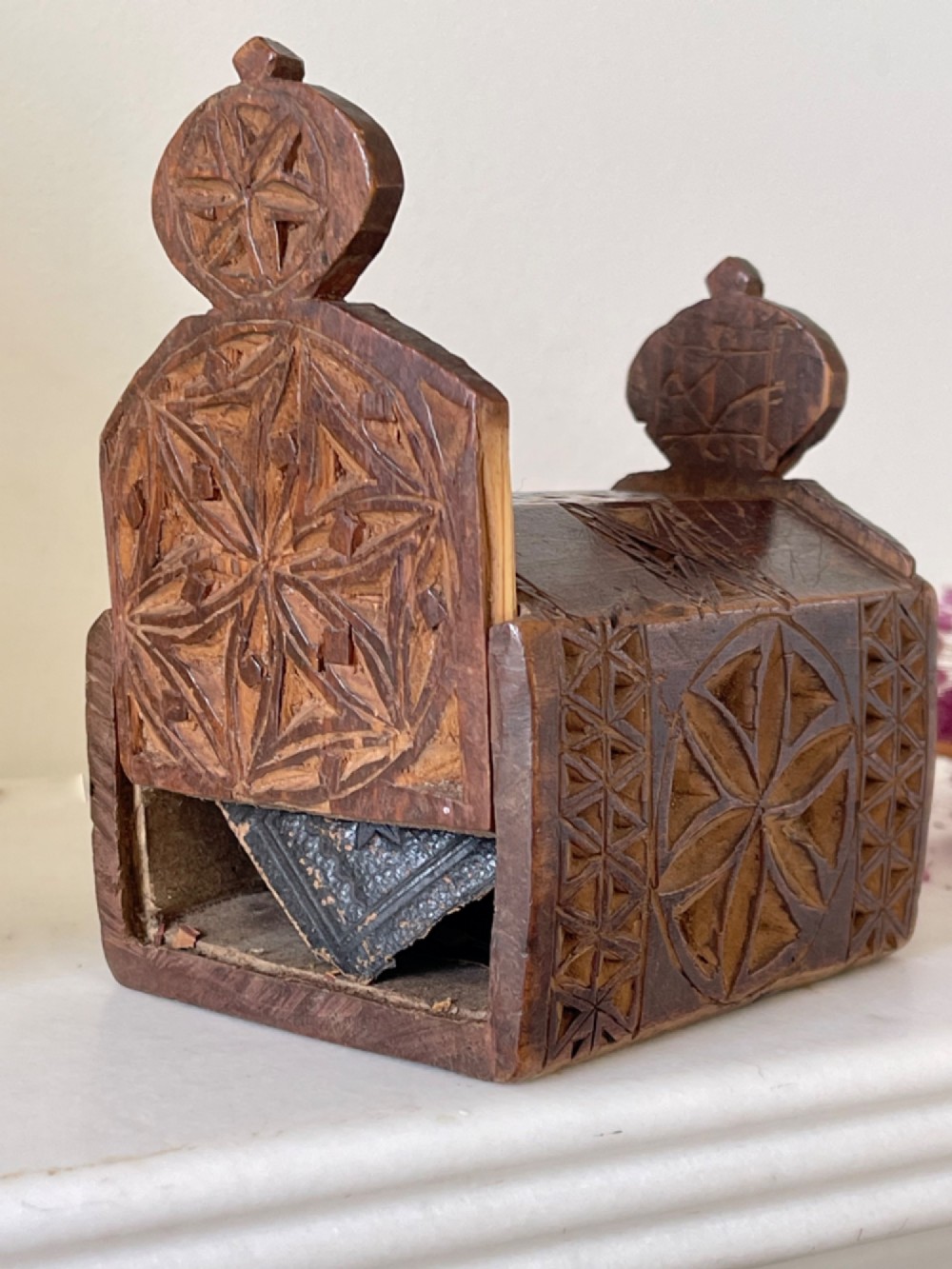 A small hand-carved warm brown wooden box featuring geometric chip-carved starburst motifs and upright carved finials. View V