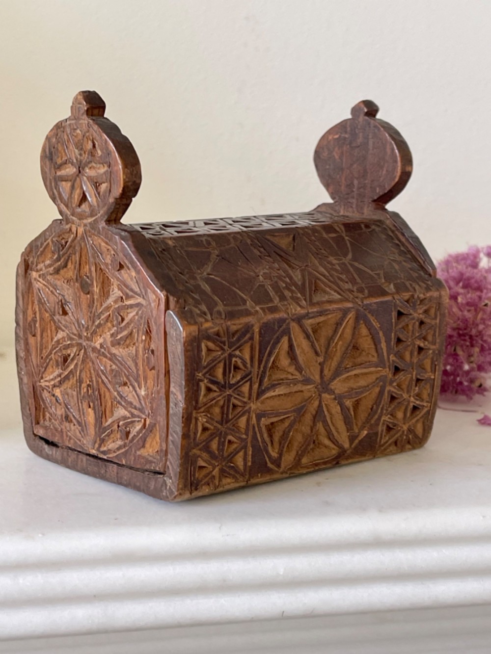 A small hand-carved warm brown wooden box featuring geometric chip-carved starburst motifs and upright carved finials. View VI
