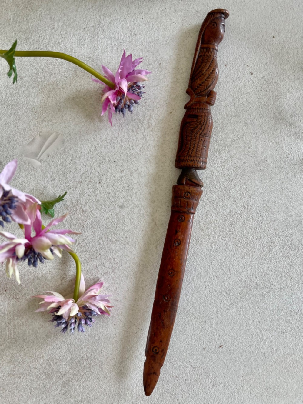 A hand-carved brown wooden knitting sheath decorated with a figurative bird motif at the top and incised geometric circles along the body.