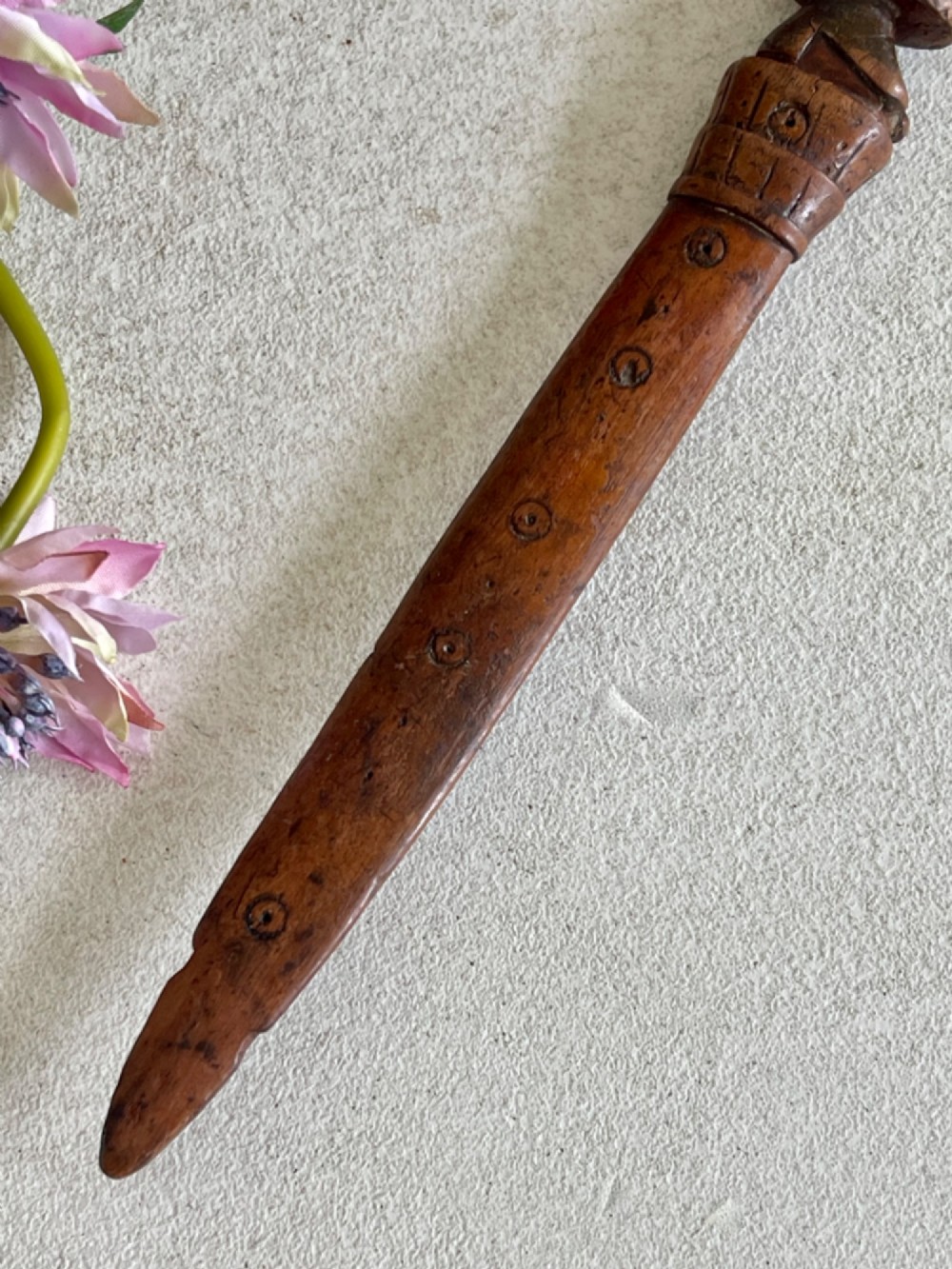 A hand-carved brown wooden knitting sheath decorated with a figurative bird motif at the top and incised geometric circles along the body. View VI
