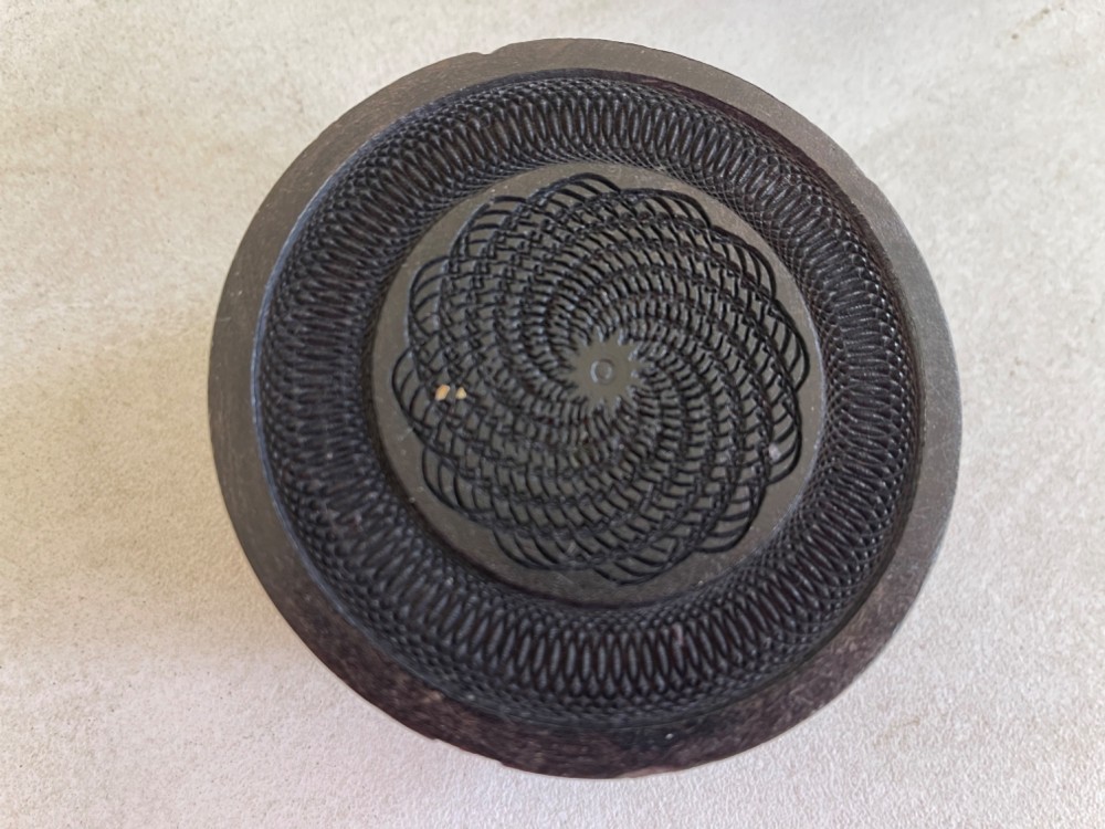 A circular dark brown engine-turned box featuring a central raised floral relief medallion on the lid. View II