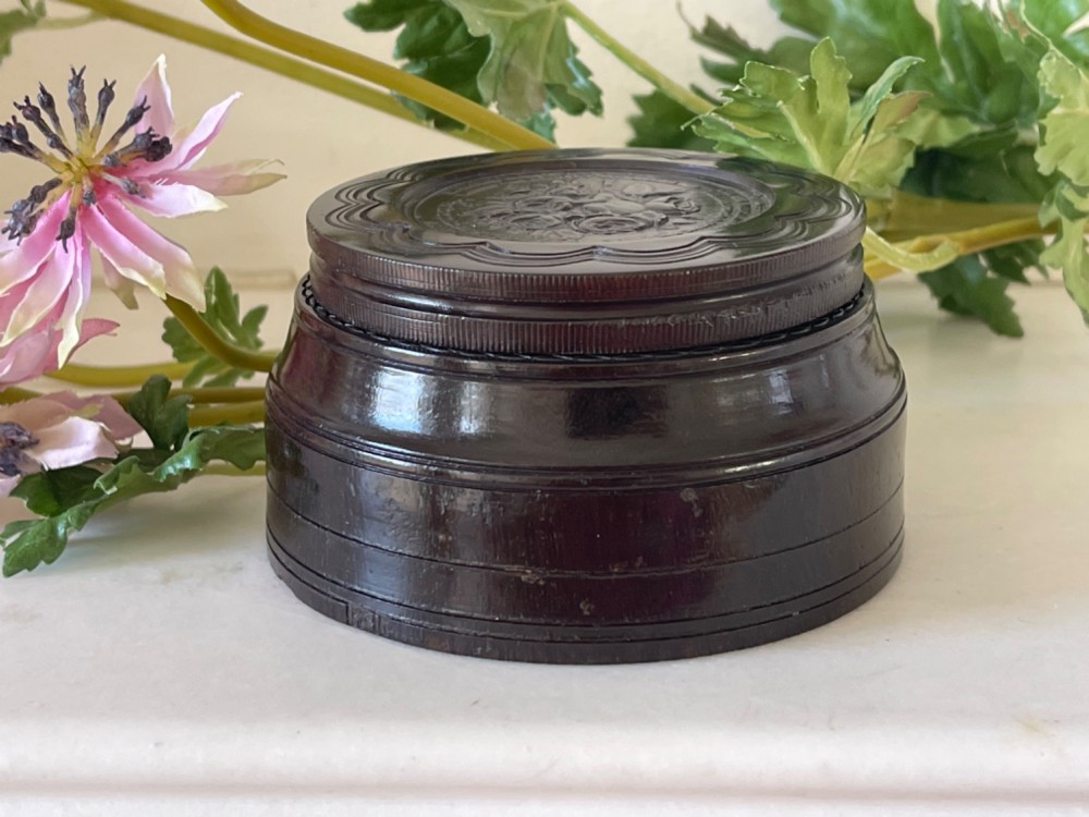 A circular dark brown engine-turned box featuring a central raised floral relief medallion on the lid. View III