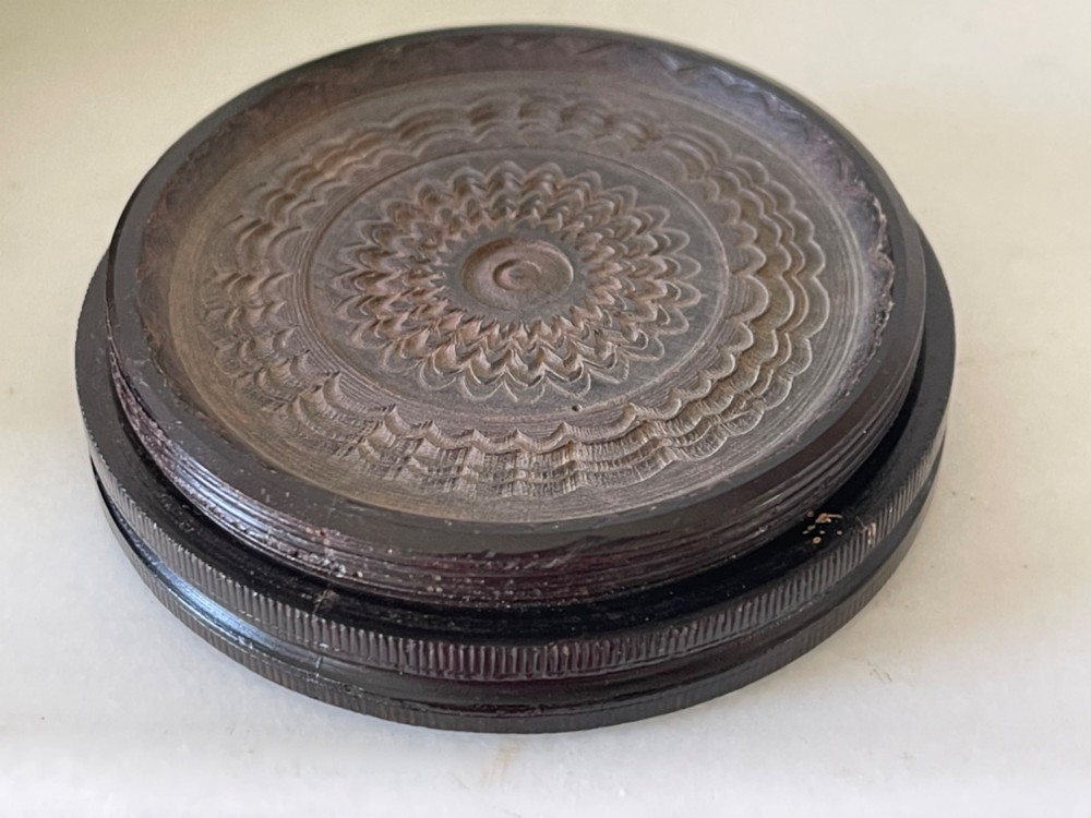 A circular dark brown engine-turned box featuring a central raised floral relief medallion on the lid. View IV