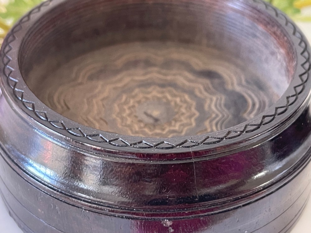 A circular dark brown engine-turned box featuring a central raised floral relief medallion on the lid. View VI