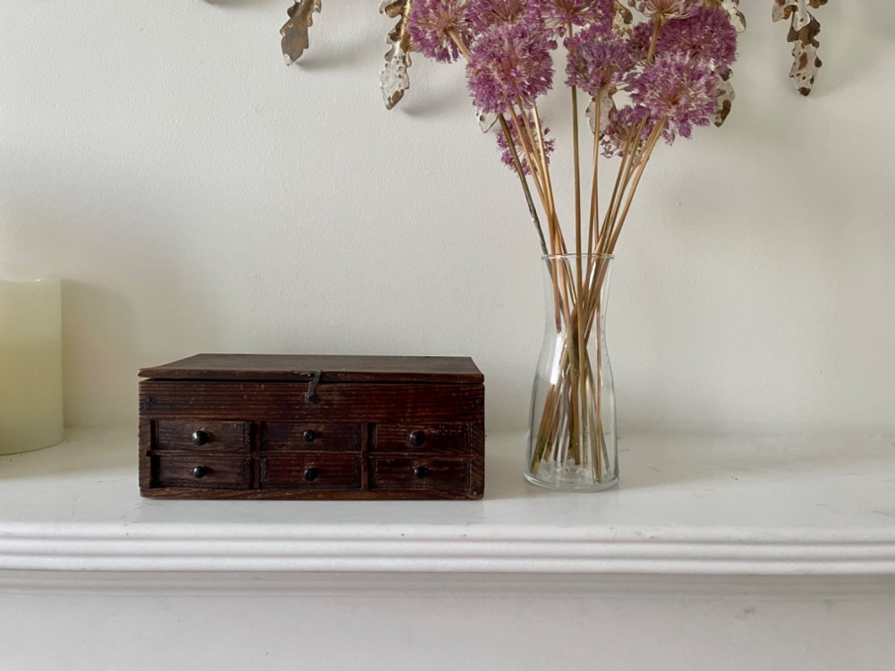 A dark pine antique watchmakers box featuring a hinged top lid, metal clasp, and six small wooden drawers with turned knobs. View IV