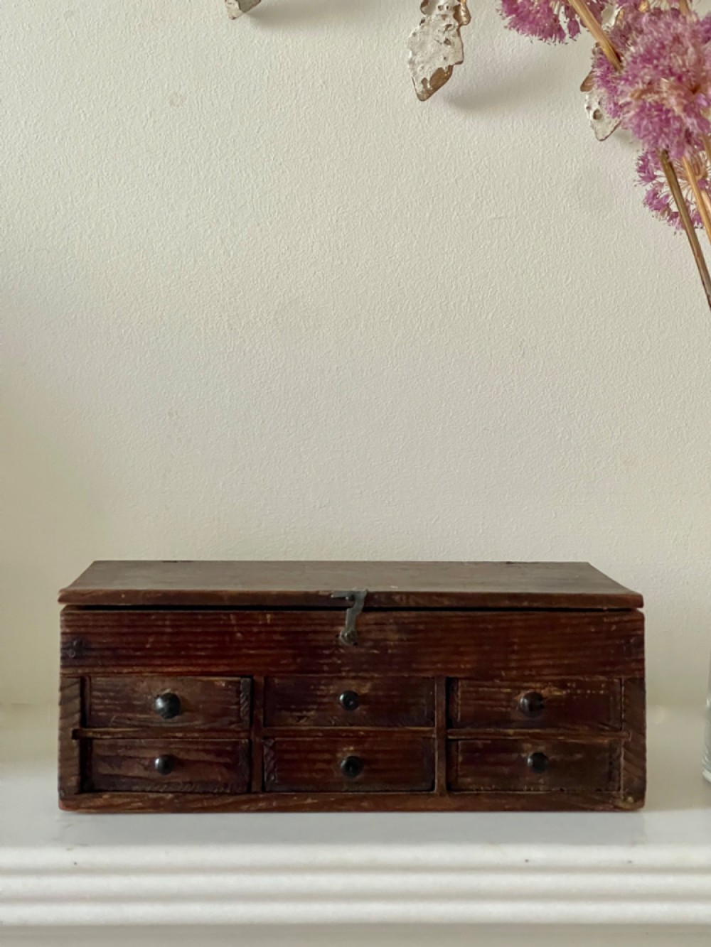 A dark pine antique watchmakers box featuring a hinged top lid, metal clasp, and six small wooden drawers with turned knobs. View V