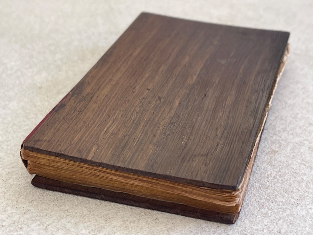 An antique small volume bound with dark wooden board covers, a worn red spine with gilt lettering, and internal pages with printed maritime engravings. View III
