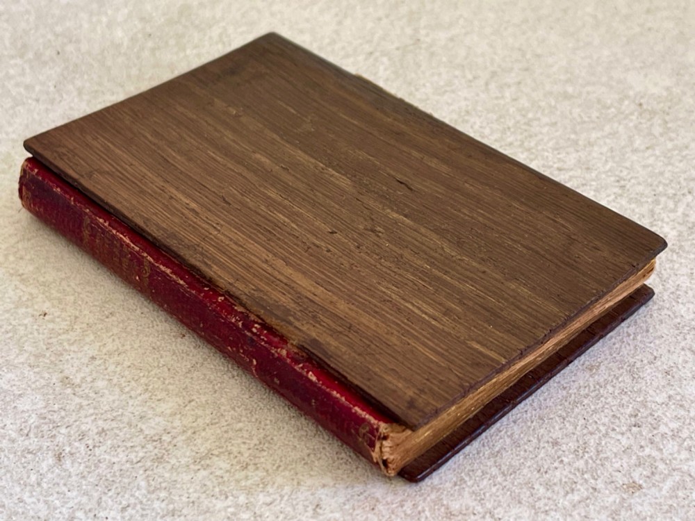 An antique small volume bound with dark wooden board covers, a worn red spine with gilt lettering, and internal pages with printed maritime engravings. View IV