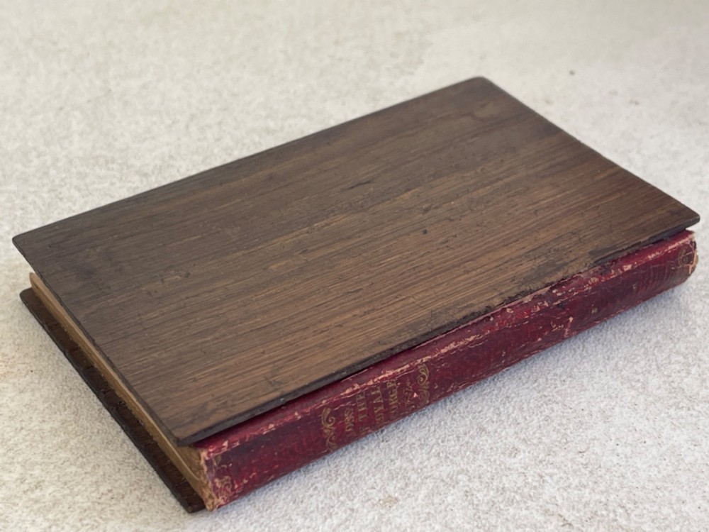 An antique small volume bound with dark wooden board covers, a worn red spine with gilt lettering, and internal pages with printed maritime engravings. View VI