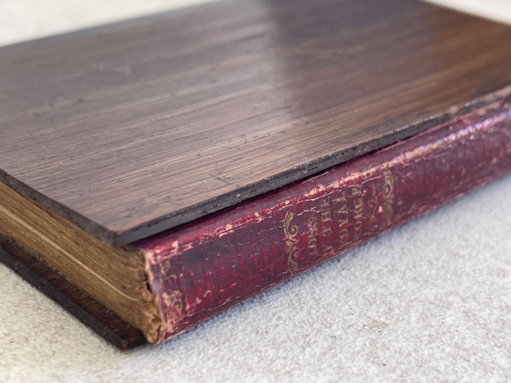 An antique small volume bound with dark wooden board covers, a worn red spine with gilt lettering, and internal pages with printed maritime engravings. View VII