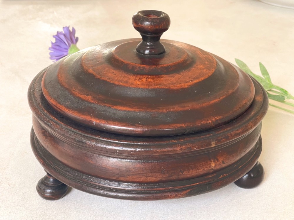 A dark turned wood circular tabletop roulette game featuring a stepped fitted lid with a turned central finial raised on bun feet.
