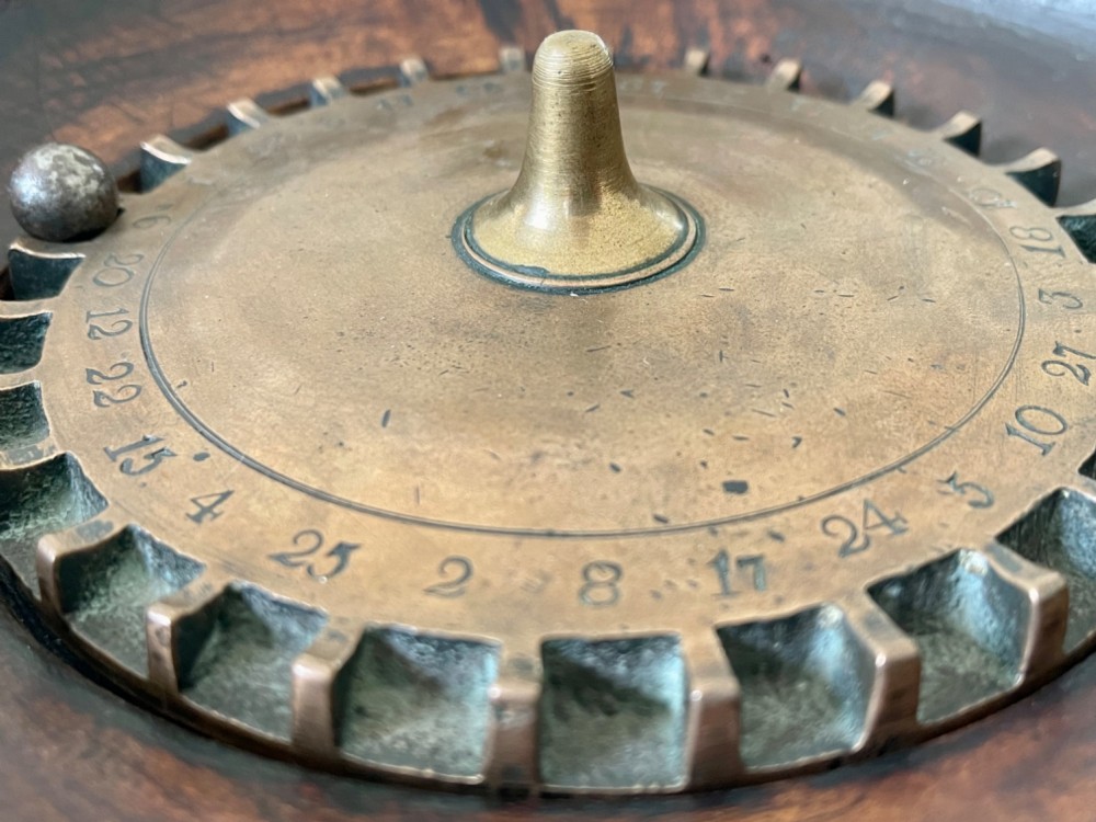 A dark turned wood circular tabletop roulette game featuring a stepped fitted lid with a turned central finial raised on bun feet. View IV