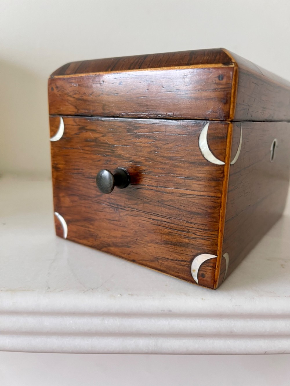 An antique rectangular rosewood box featuring a hinged lid, mother-of-pearl crescent corner inlays, and a central brass keyhole escutcheon. View III