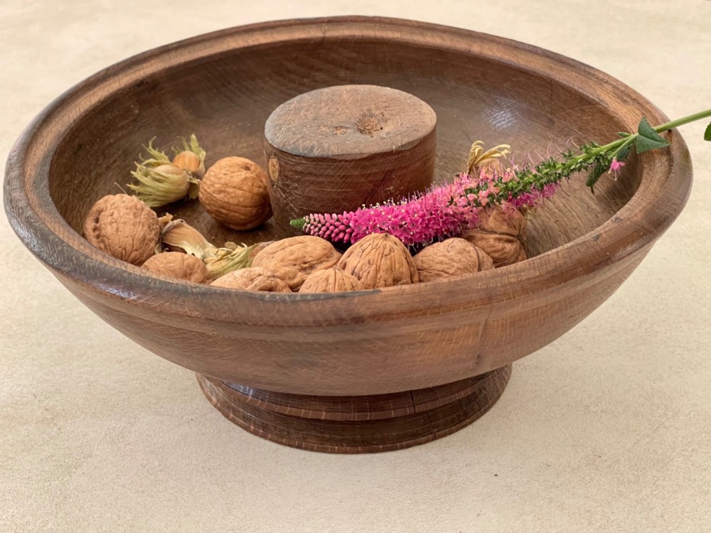 A turned dark wood pedestal bowl featuring a raised central anvil post and a stepped circular base.