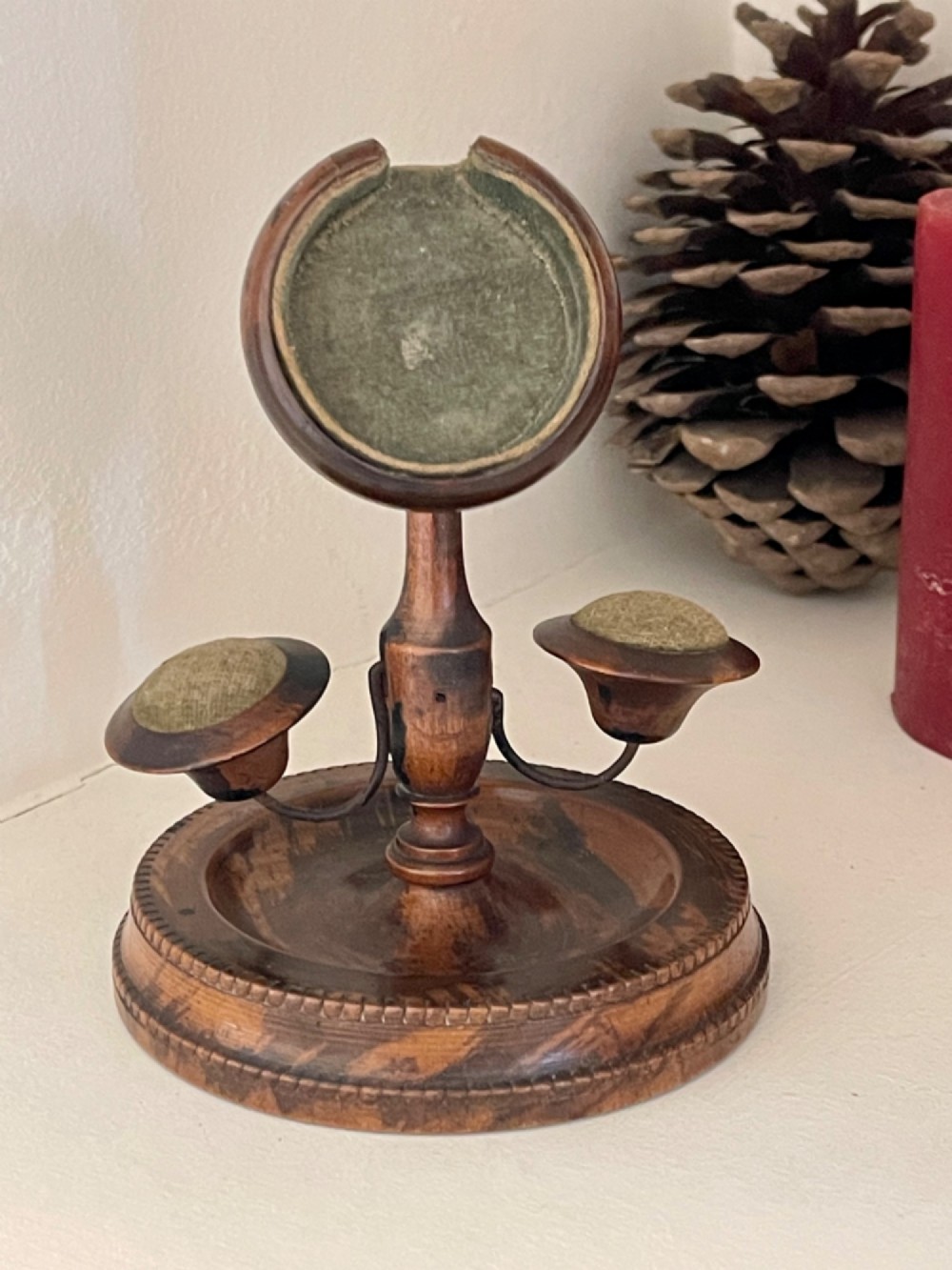 An antique turned wood pocket watch stand with a green velvet lined circular holder and two integrated side pincushions on a dished base. View II
