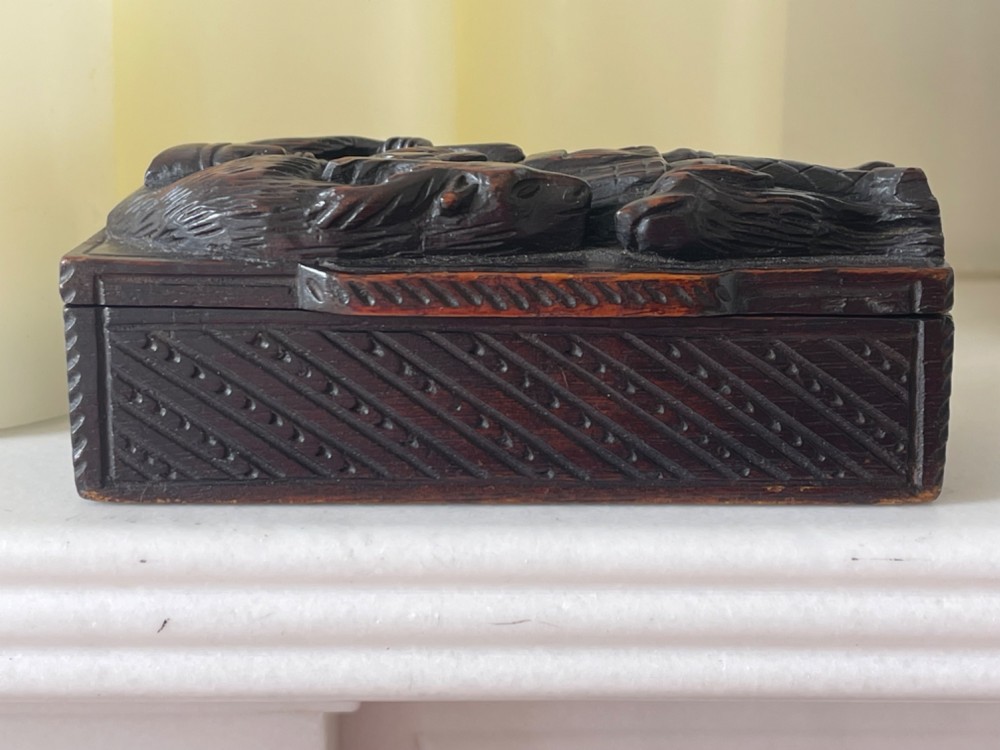 A dark carved wooden table snuff box lid depicting a Scottish Highlander in a kilt carrying a stag across his shoulders with a hound at his feet. View V