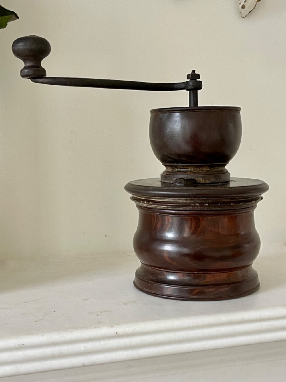 A turned dark brown lignum vitae coffee grinder with a curved iron crank handle and turned wooden knob.