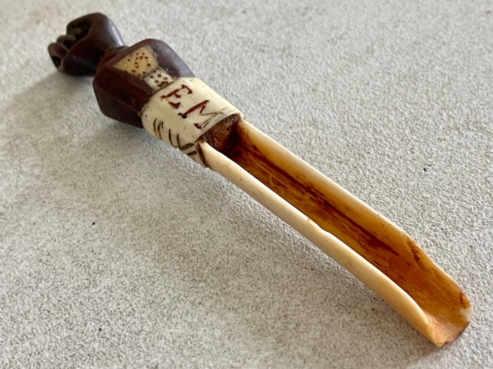 A carved antique bone and wooden apple scoop featuring a terminal in the shape of a clenched fist and carved lettering on the collar.