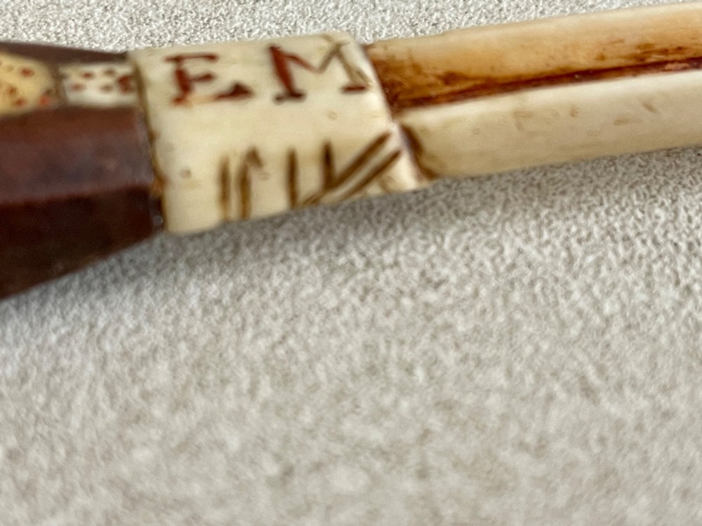 A carved antique bone and wooden apple scoop featuring a terminal in the shape of a clenched fist and carved lettering on the collar. View IV