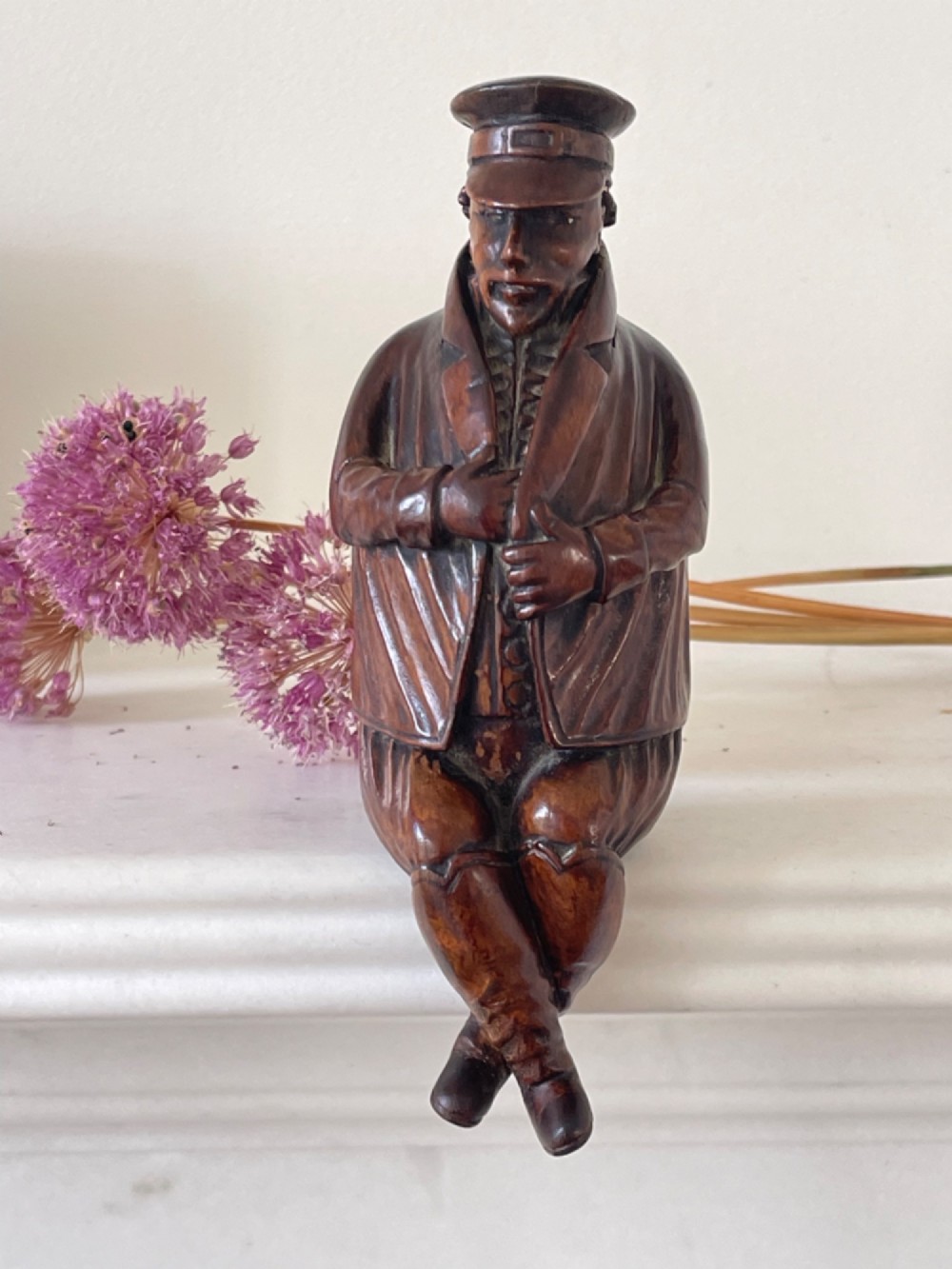 A hand-carved dark wood treen snuff box shaped as a seated man wearing a peaked cap and coat with his legs crossed.