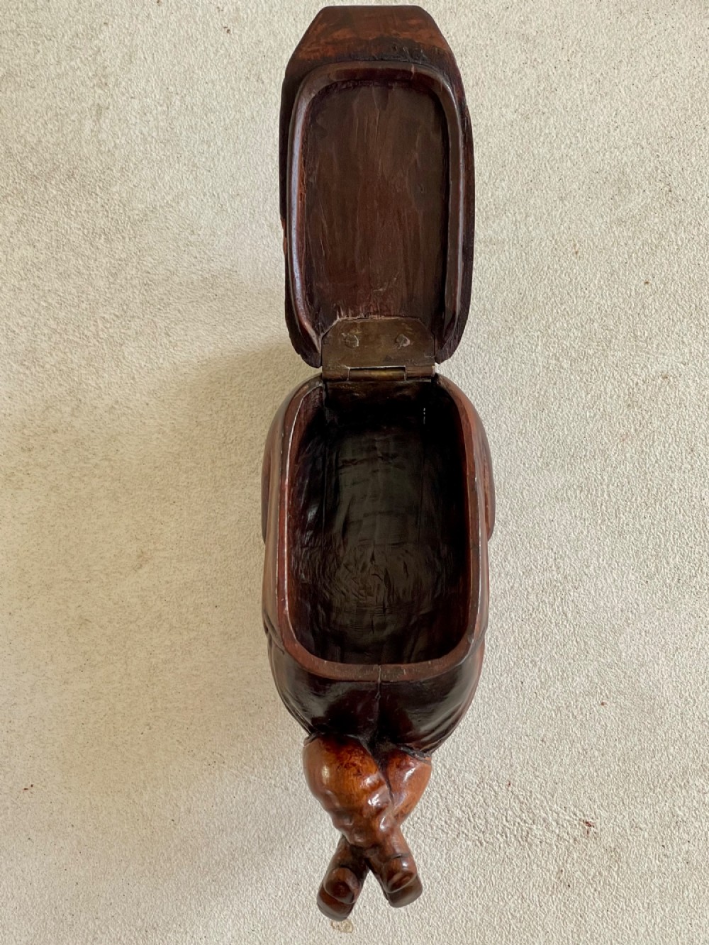 A hand-carved dark wood treen snuff box shaped as a seated man wearing a peaked cap and coat with his legs crossed. View II