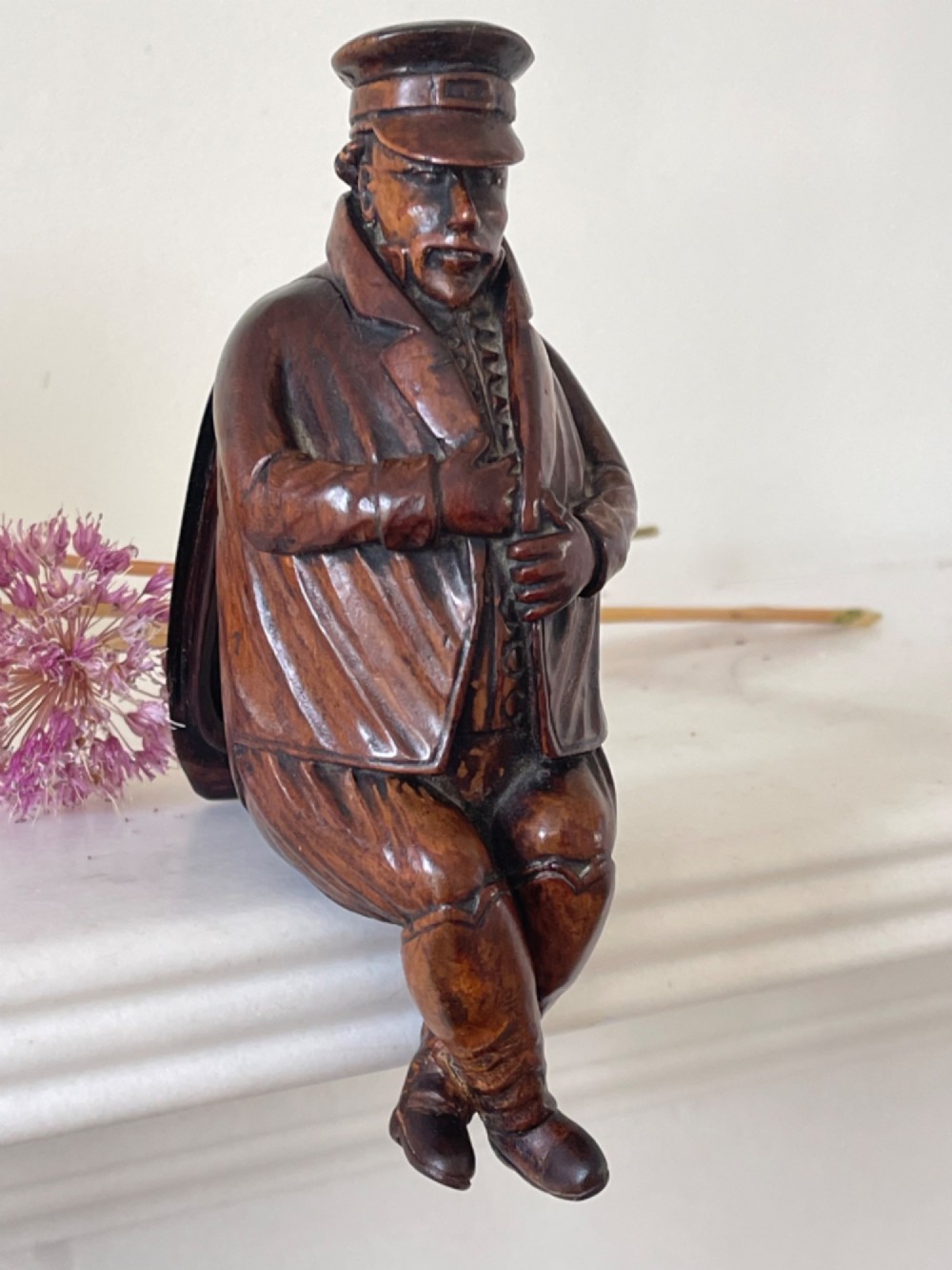 A hand-carved dark wood treen snuff box shaped as a seated man wearing a peaked cap and coat with his legs crossed. View IV
