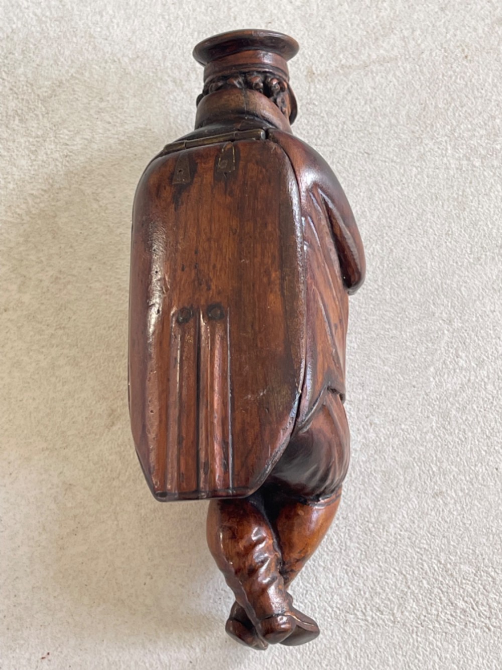 A hand-carved dark wood treen snuff box shaped as a seated man wearing a peaked cap and coat with his legs crossed. View V