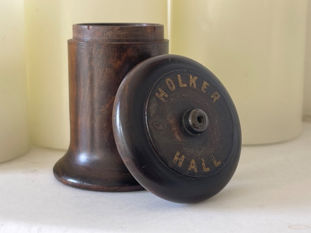A small turned dark wooden go-to-bed match holder featuring a cylindrical body, a moulded cap, and a match inserted in the centre top. View II