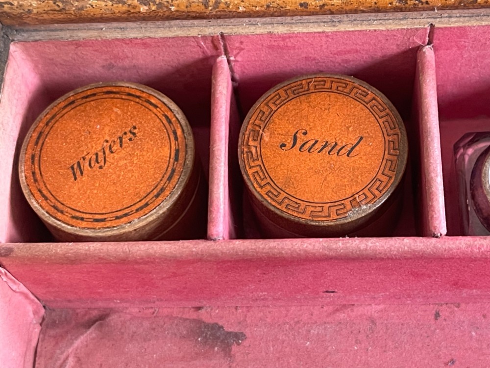 A rectangular wooden box lid featuring a central circular printed vignette of a country house surrounded by geometric green and black borders on an ochre surface. View VI