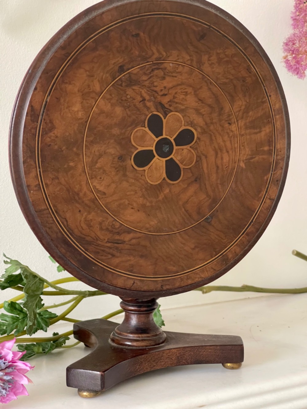 An antique circular tilt-top table featuring burr walnut veneer with a central floral marquetry inlay on a turned pedestal and triform base. View IV