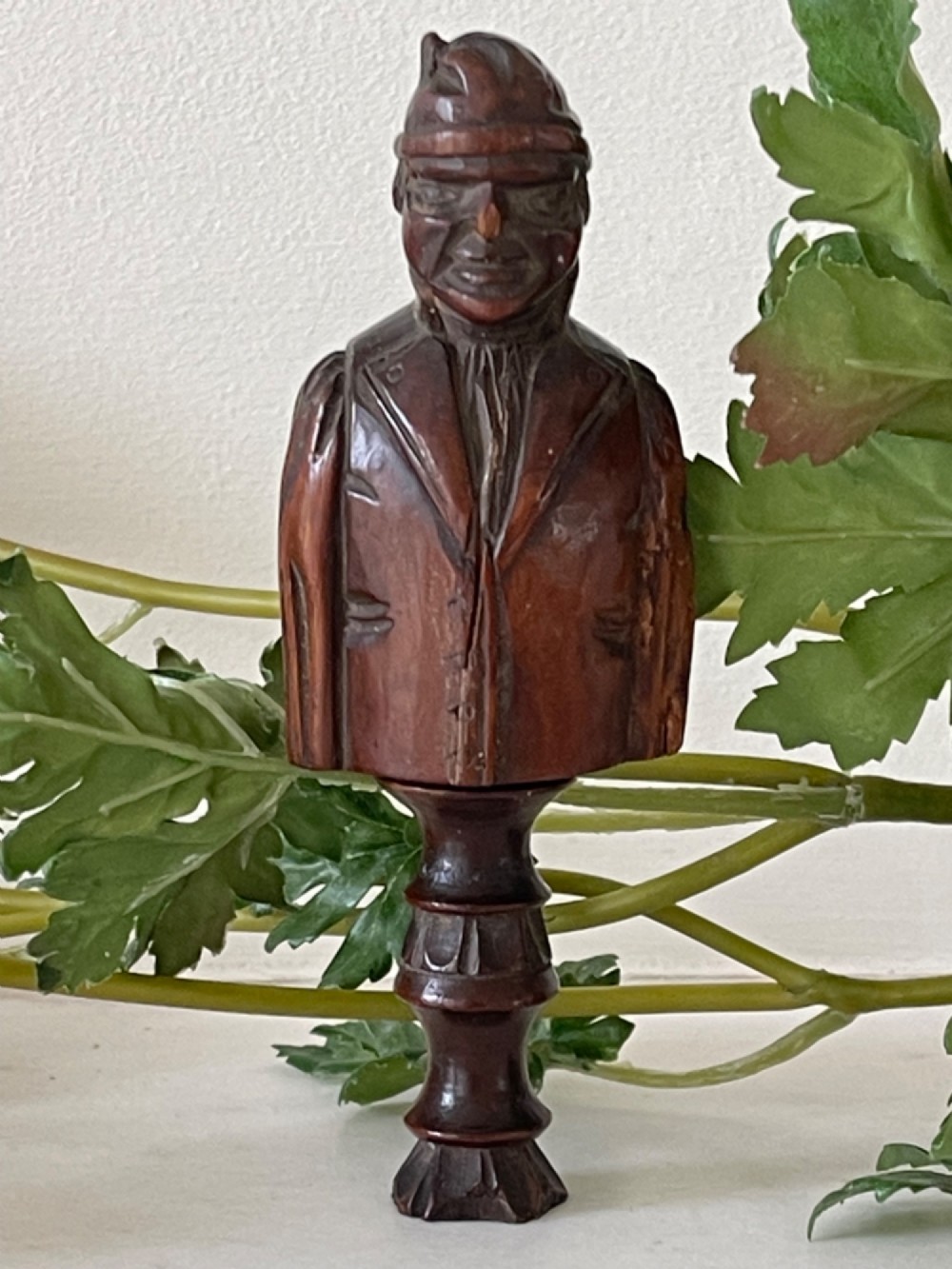 A dark carved wooden treen nutcracker featuring a male bust wearing a cap and jacket atop a turned pedestal handle. View III